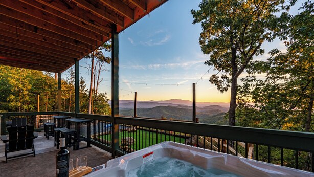 Un bain à remous doté d’une terrasse en bois et de sièges extérieurs, offrant une vue sur un paysage montagneux.