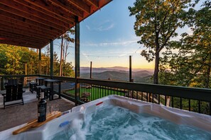Un bain à remous doté d’une terrasse en bois et de sièges extérieurs, offrant une vue sur un paysage montagneux.