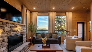 Un salon chaleureux avec une cheminée en pierre, un canapé sombre et un plafond en bois.