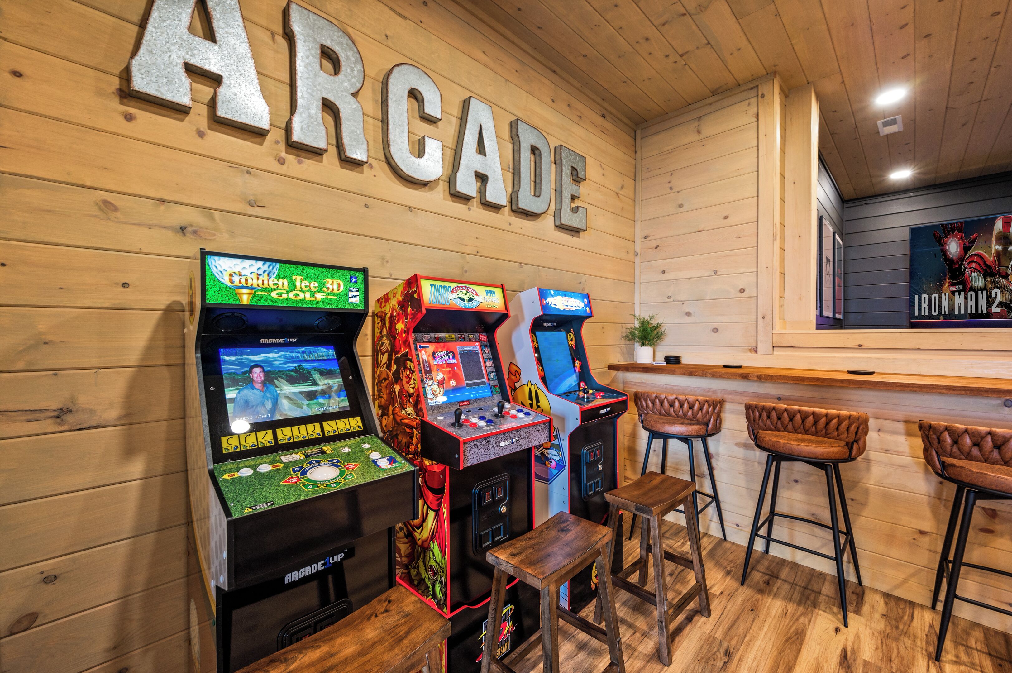 Arcadespellen, houten barkrukken en een muur met de tekst 'ARCADE' in een rustieke omgeving.