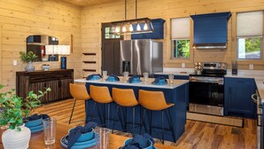 Une cuisine moderne avec des murs en bois, un îlot central doté de tabourets de bar, des appareils en acier inoxydable et un luminaire suspendu.