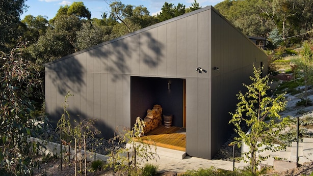 Um edifício moderno e minimalista, com uma entrada ampla e aberta, rodeado por vegetação natural e um terreno inclinado.