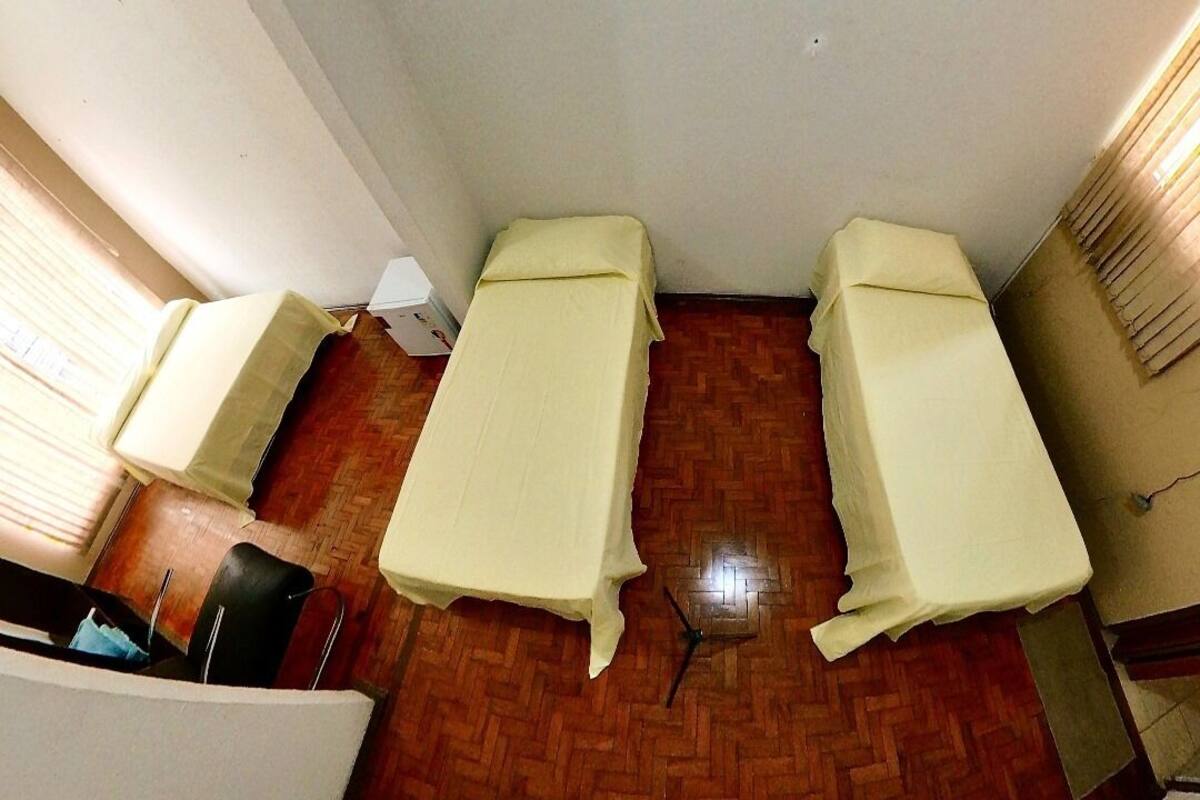 A room with two beds covered in white sheets, a wooden floor, and a window with curtains.