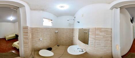 Un baño con un lavamanos grande, un espejo y una ducha. Hay una ventana y una puerta que da a otra habitación.