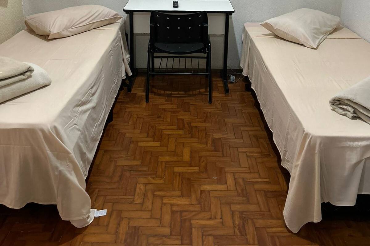 A small, clean room with two single beds, a desk, and a chair.