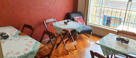 Un comedor con mesas y sillas de madera, una pared roja y vistas al exterior a través de una ventana con barandilla de metal.