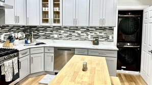 A modern kitchen with grey cabinets, a stainless steel range, a wooden table, and a built-in washer and dryer. - Family Retreat - Stunning 5BR-2BA with Parking/ Near Savin Hill Station (Boston)