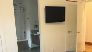 Un dormitori amb un llit, un televisor fixat a la paret i un bany visible a través d'una porta oberta.
