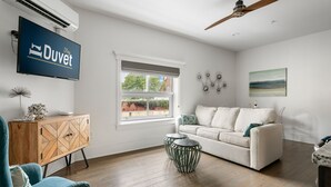 A modern living room with a white sofa, a blue armchair, a wooden cabinet, and a television displaying 'Duvet Stay'.