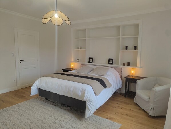 Une chambre à coucher comprenant un lit, des tables de chevet, une chaise, un luminaire suspendu et des étagères intégrées.