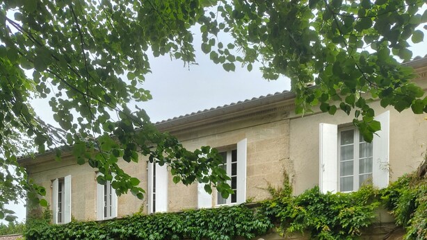 A building with a long table and chairs set up outside, a green door, and a stone facade.