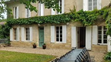 Un bâtiment avec une longue table et des chaises disposées à l’extérieur, une porte verte et une façade en pierre.