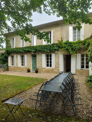 A building with a long table and chairs set up outside, a green door, and a stone facade. - Large house with 14 beds, swimming pool overlooking vineyards between Blaye and Bordeaux (Gauriac)