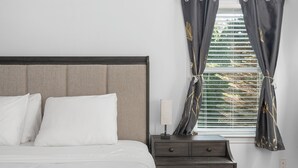 A neatly made bed with white linens, a dark wooden headboard, and a bedside table with a lamp and a small drawer. - Near Newport, Beaches, Golf & Navy Base (Middletown)
