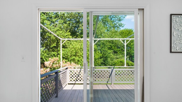 A room with a sliding glass door leading to an outdoor deck with a wooden floor and white lattice railing. - Near Newport, Beaches, Golf & Navy Base (Middletown)