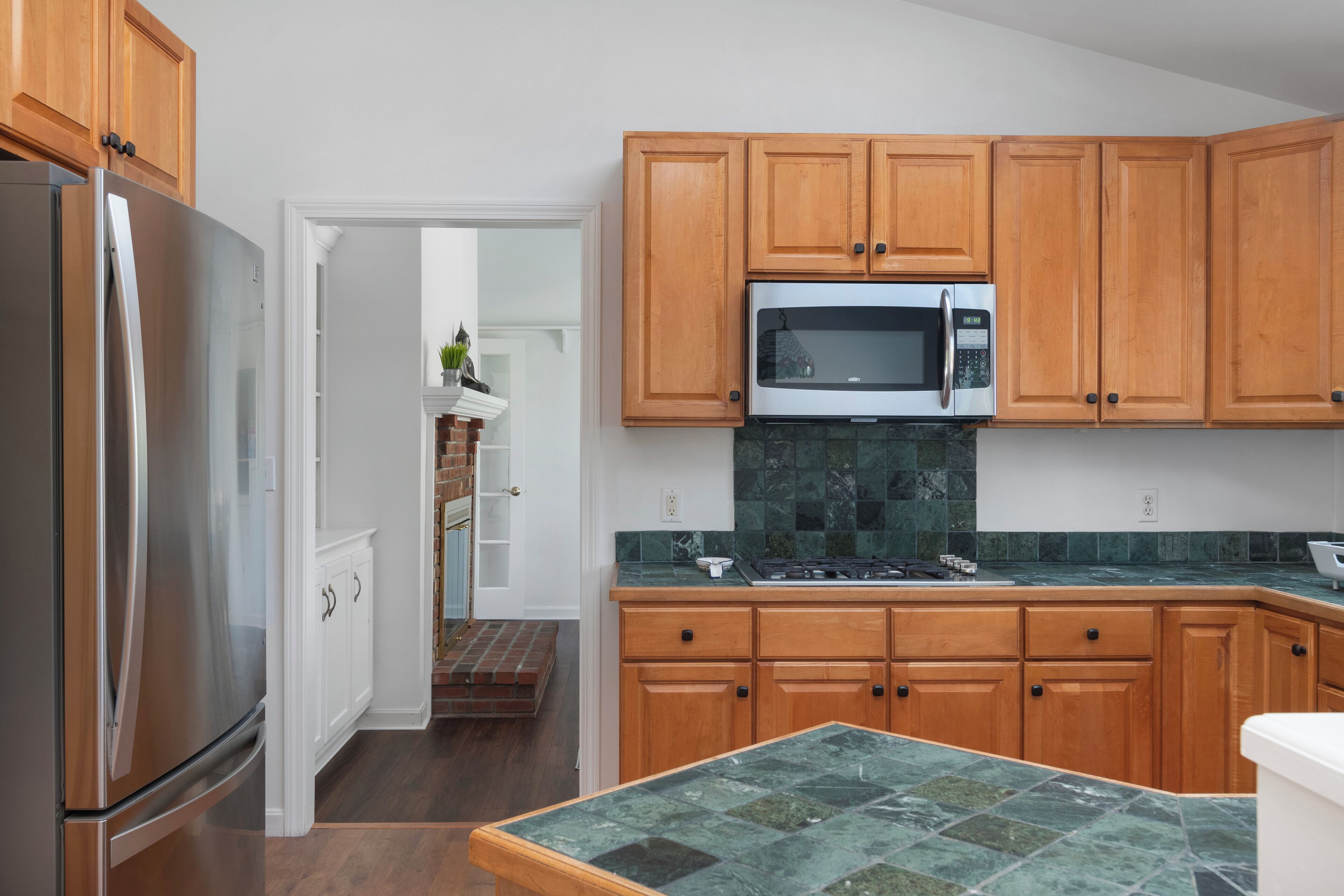 Una cocina con armarios de madera, un refrigerador de acero inoxidable, un microondas y un salpicadero de azulejos verdes.