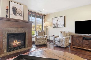 A living room with a fireplace, two armchairs, a television, and artwork on the walls.