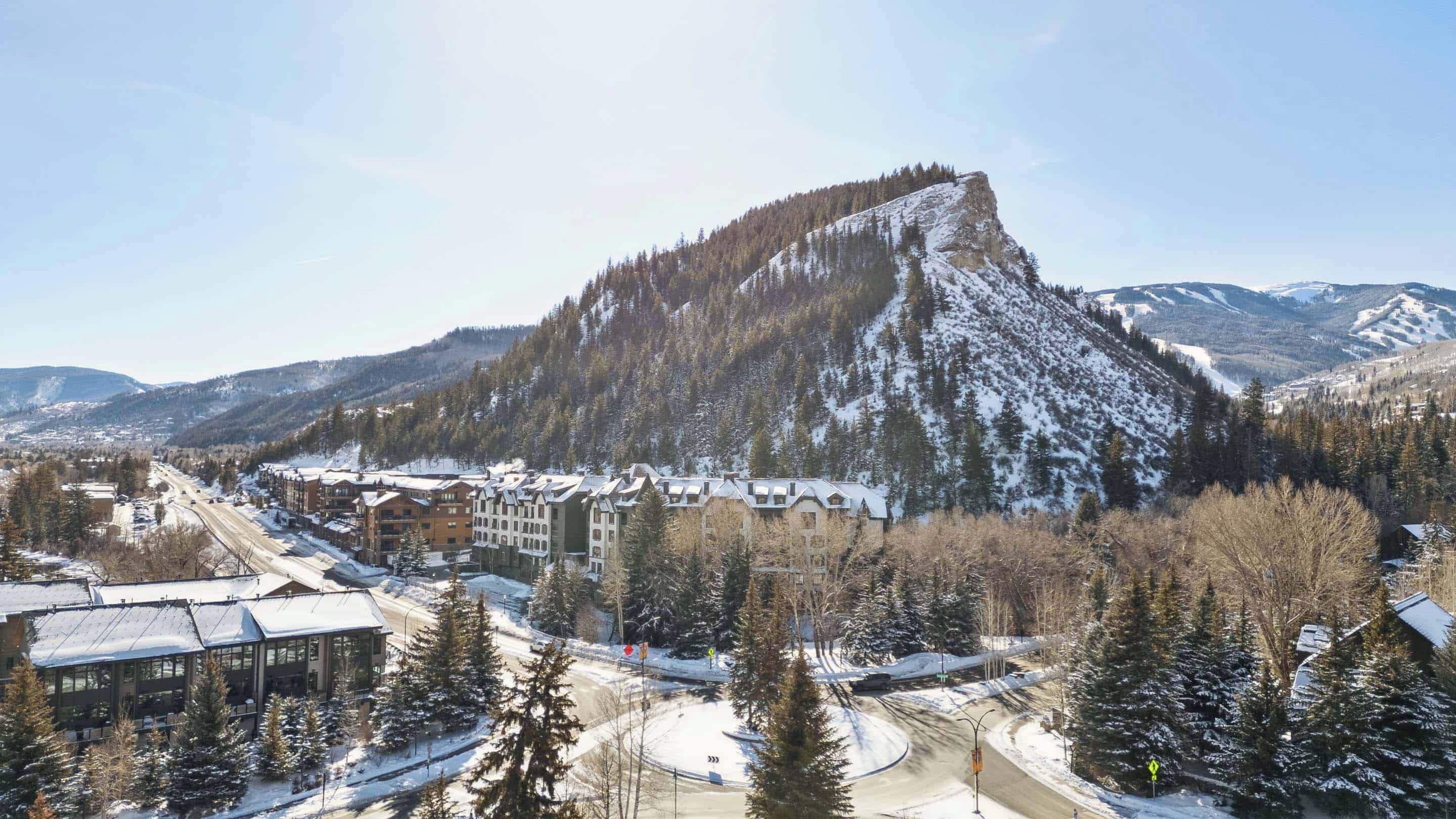 A ski resort with a prominent mountain, buildings with snow-covered roofs, and a clear sky.
