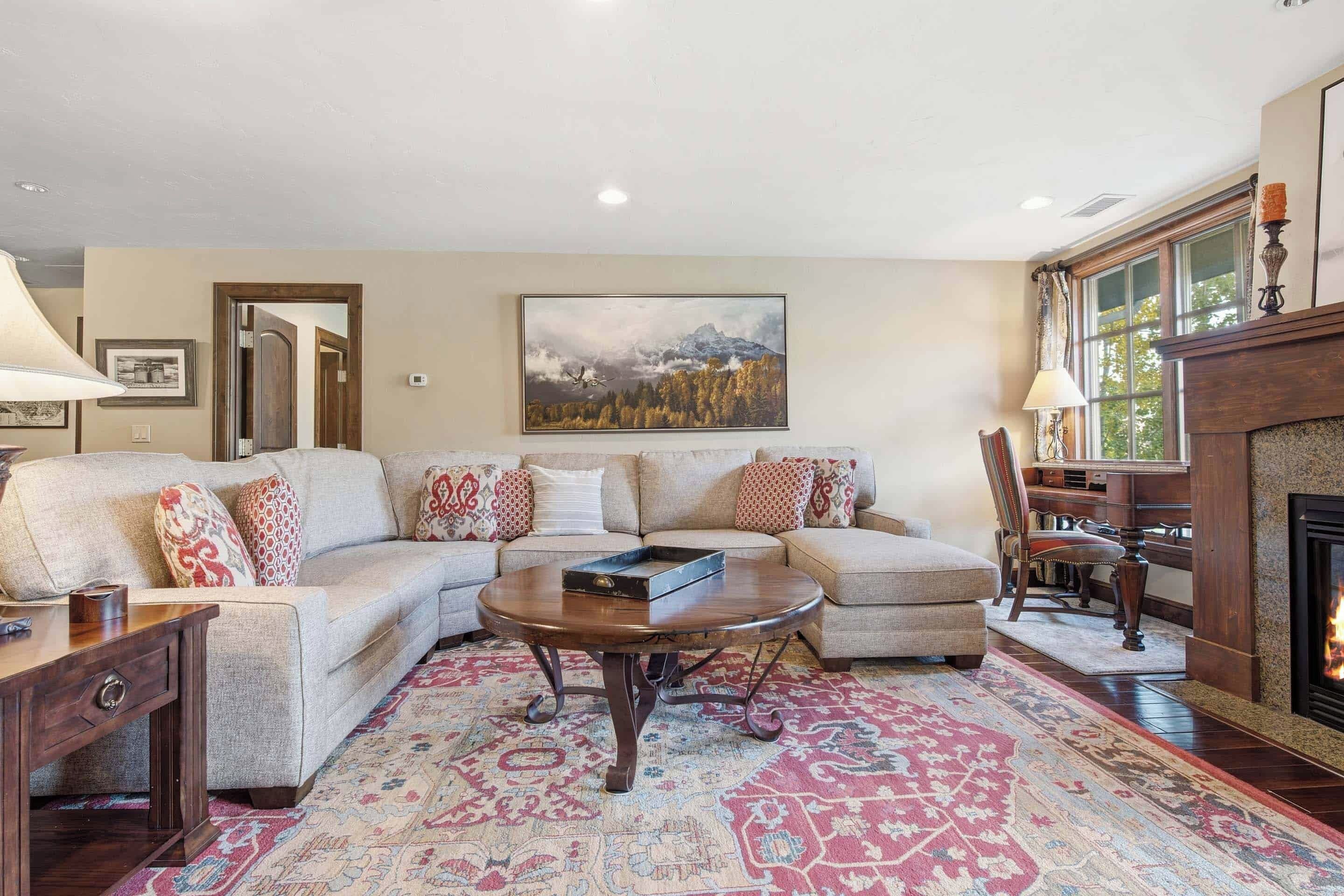 A living room with a sectional sofa, a coffee table, a fireplace, and a large landscape painting on the wall.