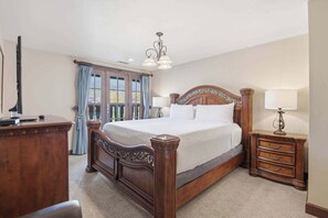 A bedroom with a large wooden bed, two bedside tables with lamps, a dresser, and a window with curtains.