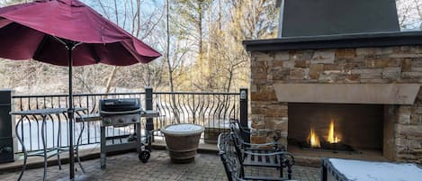 An outdoor patio with a stone fireplace, a grill, and a bench.