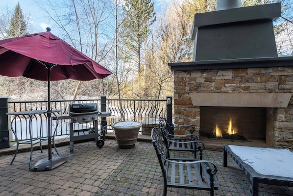 An outdoor patio with a stone fireplace, a grill, and a bench.