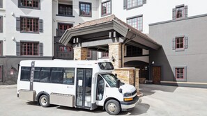 A white bus parked in front of a building with multiple windows and a stone facade.