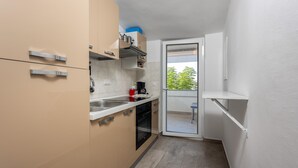 Et lille køkken med vask, komfur og skabe, der fører ud til en balkon med udsigt til træer.