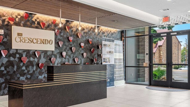 A reception desk with a sign reading 'The Crescendo,' a patterned wall, and a view of the outside through glass doors. - Luxury Music Row Condo | King Bed & Balcony (Nashville)