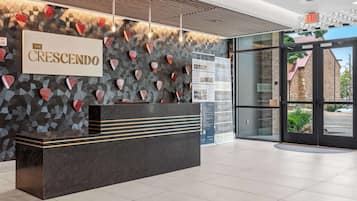 A reception desk with a sign reading 'The Crescendo,' a patterned wall, and a view of the outside through glass doors.