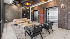 A modern lobby with a sofa, chairs, a coffee table, a patterned wall, and an elevator. - Luxury Music Row Condo | King Bed & Balcony (Nashville)