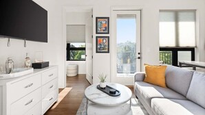 A modern living room with a flat-screen TV, white cabinetry, a gray sofa, and a large window with a view. - Luxury Music Row Condo | King Bed & Balcony (Nashville)