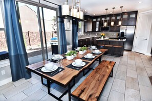 A modern kitchen with dark cabinetry, stainless steel appliances, and a large dining table set for six.