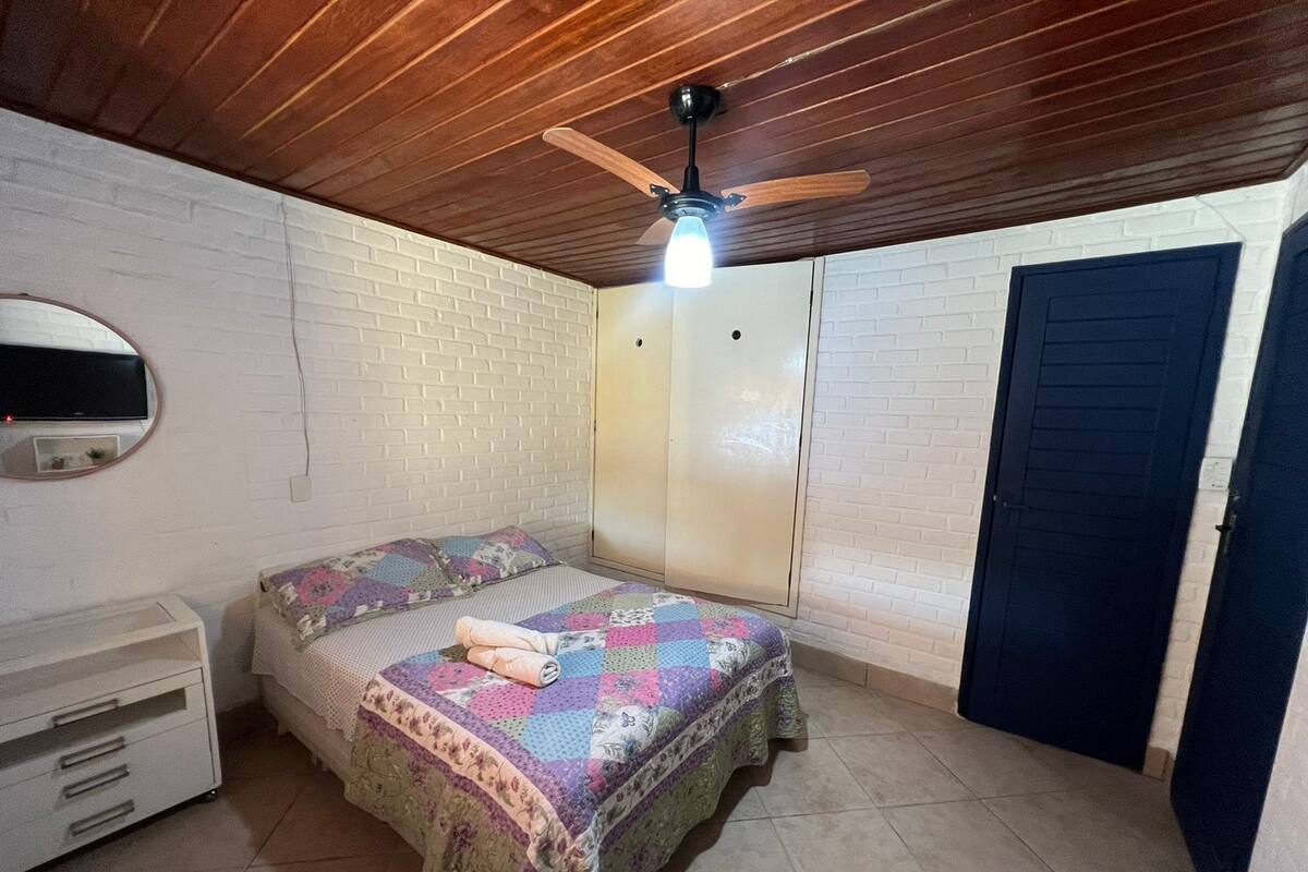 A bedroom with a bed, a wardrobe, a ceiling fan, and a TV mounted on the wall.