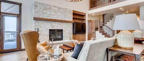A spacious living area with a fireplace, a high ceiling, and a staircase leading to an upper level.