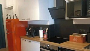 Une cuisine de taille réduite avec des meubles blancs, un réfrigérateur rouge et une hotte noire.