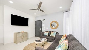 A modern living room with a grey sofa, a round coffee table, a TV mounted on the wall, and a ceiling fan. - Los Mangos #3 • NEW! 3 BR Town-home • Private Plunge Pool Terrace, Coco Beach • Guests (Playa Hermosa)