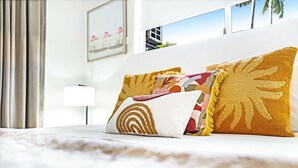 Una cama bien hecha con varias almohadas, una lámpara y un cuadro en la pared.