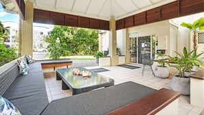 Un espacio de estar al aire libre techado, con mostrador de recepción, sofá y una mesa decorada con flores.