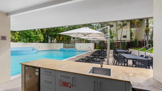 Zona junto a la piscina con estación de barbacoa, asientos exteriores y vistas a la piscina.