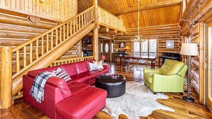 Un interior de cabaña de madera espacioso con un sofá de cuero rojo, un sillón verde, una escalera de madera y un comedor.