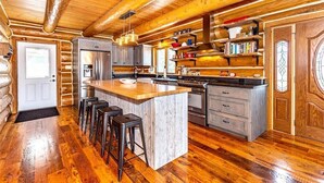 Cocina estilo cabaña de troncos con una isla central, taburetes de bar y suelo de madera.