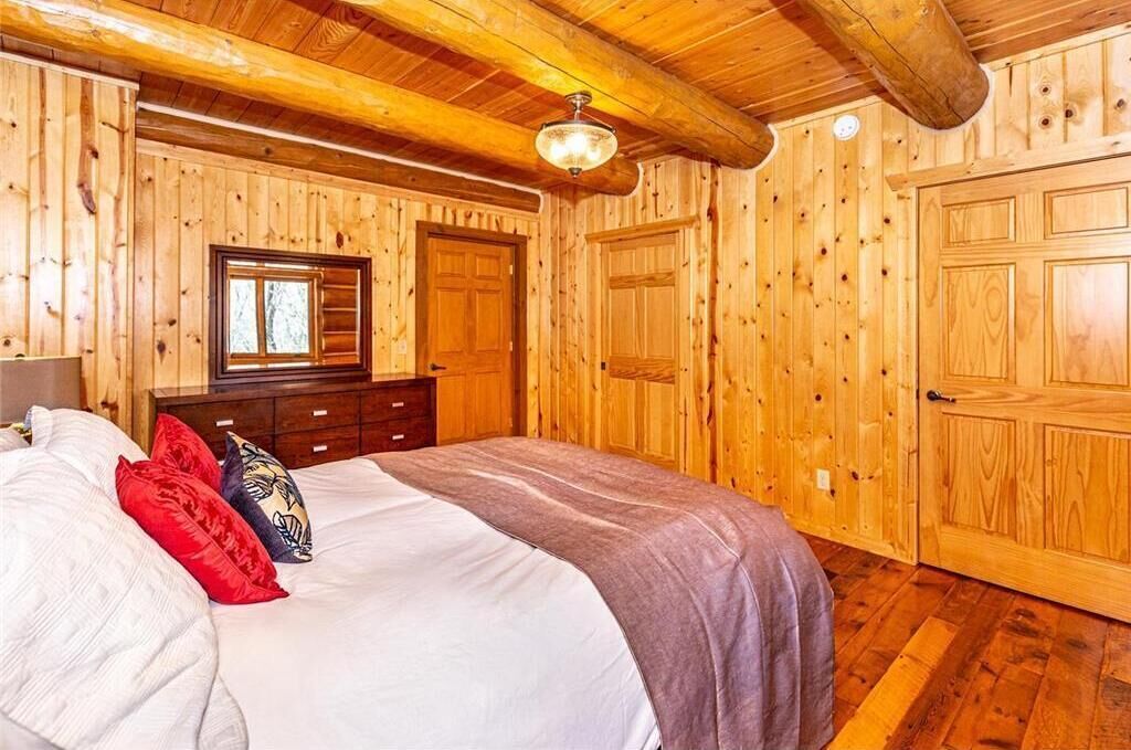 Quarto com paredes de madeira, uma cama, cômoda e duas portas.