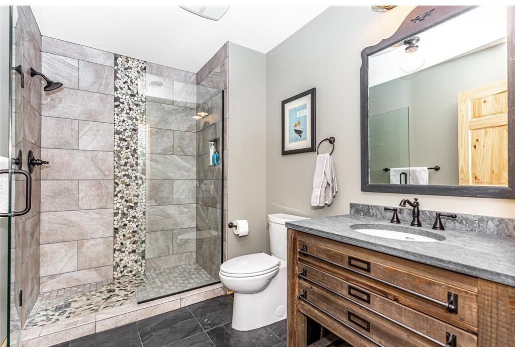 A modern bathroom with a glass-enclosed shower, a toilet, a sink with a wooden vanity, and a large mirror.