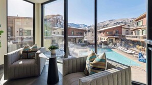 A modern hotel room with large windows overlooking a pool and mountains. There are two sofas with patterned cushions and a small table with a plant. - One Riverfront Townhome 05 (Avon)