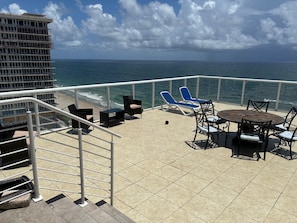 Un balcon avec vue sur l’océan, des fauteuils bleus, une table ronde et un escalier.