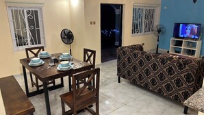 Un comedor con una mesa lista para cuatro personas, un sofá y un televisor en la sala.