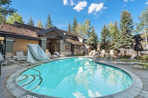 A swimming pool with a tiled edge, lounge chairs, and a covered patio area.