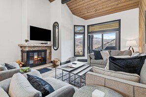 A modern living room with a stone fireplace, a flat-screen TV, and a large window offering a mountain view. - Ridgepoint Townhome 086 - 3 Bedroom plus Loft Residence (Beaver Creek)