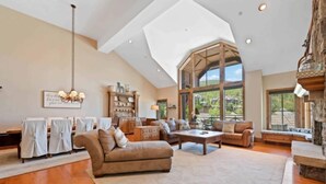 A spacious living room with a high ceiling, a large window offering a view of the outdoors, and a fireplace.